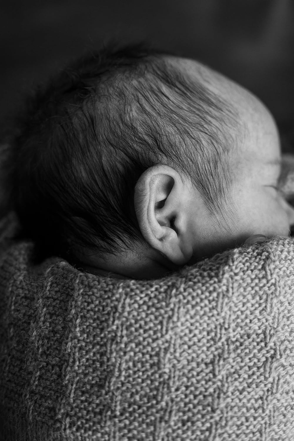 Nærbillede i sort-hvid af en lille babys øre og bløde hår, svøbt i strik. Mødregruppe- og babyfotografering i Randers og Østjylland.