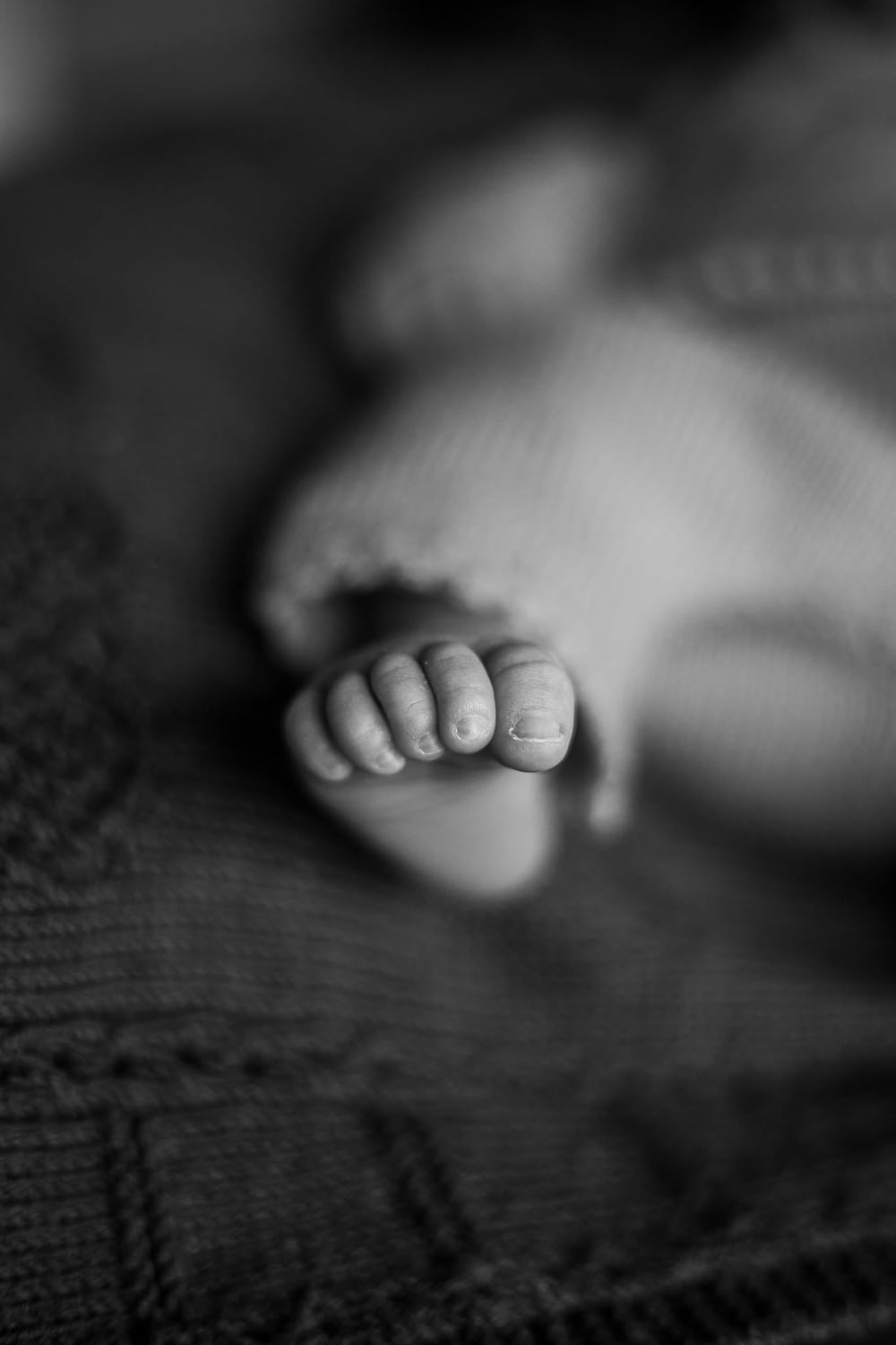Sort-hvidt detaljebillede af en babys små tæer mod et strikket tæppe. Nærværende fotografering af mødregrupper og de mindste.